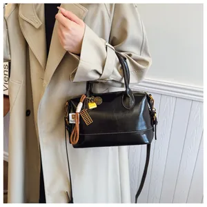 Detail of black glossy Boston bag with white stitching and vintage charms for women