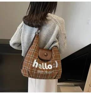 Detailed embroidery of 'hello' and leather flap on brown checkered canvas shoulder bag