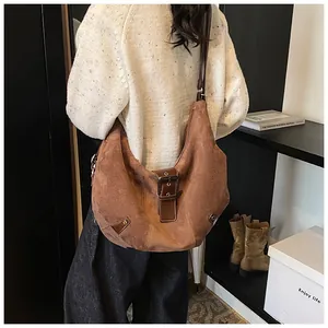 Detail of a large brown suede Hobo shoulder bag worn by a model in a retro urban setting