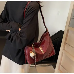 Detail view of burgundy glossy tote bag with golden buckle and plush pompom charm