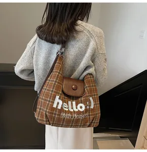 Detail of plaid canvas and leather patchwork shoulder bag with white embroidery text