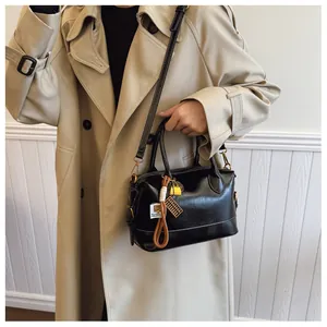 Detail of black vintage Boston bag with gold lock and abacus pendant on beige trench coat