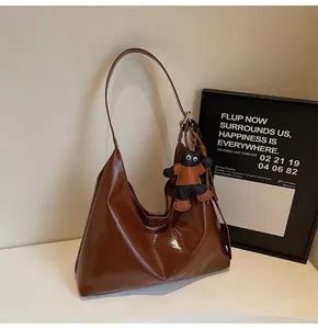 Detail of glossy brown patent leather tote bag featuring a cute cartoon cat bag charm