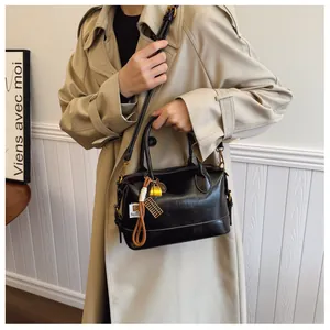 Detail of vintage black Boston bag with decorative charms and gold lock on beige coat