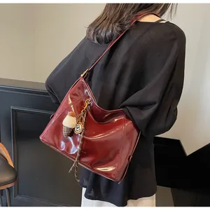 Detail view of burgundy patent leather shoulder bag with a vintage metal pendant accessory