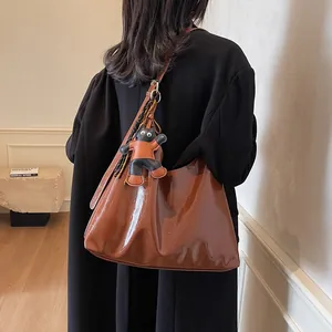 Brown patent leather tote bag with cartoon cat charm on a model's shoulder for daily commute