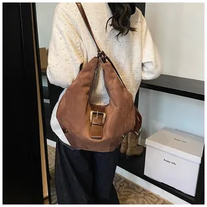 Close-up of vintage brown suede hobo bag with metal buckle and rivet detail worn by model
