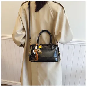 Detail of a black leather Boston bag with gold hardware and woven charm on a trench coat