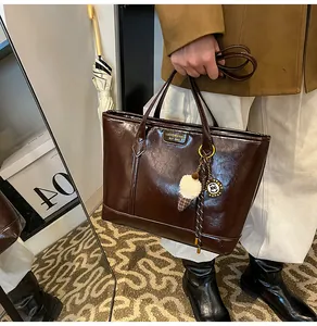 Détail d'un cabas marron foncé brillant avec logo métallique et pendentif décoratif