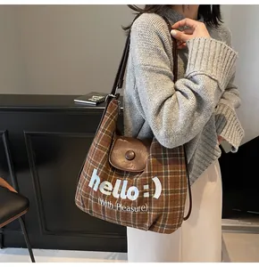 Detailed close-up of brown plaid tote bag with leather flap and hello printed slogan