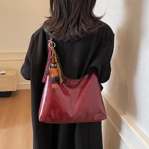 Chic burgundy patent leather oversized tote bag worn over the shoulder on black blazer