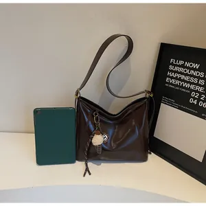 Detail of dark brown glossy shoulder bag with a plush ice cream charm and adjustable strap