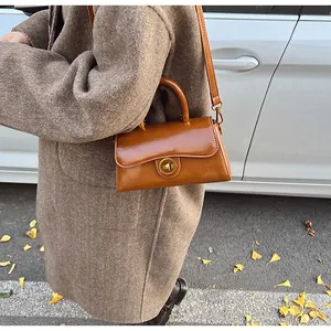 Outdoor model holding a brown polished leather vintage handbag with a gold turn-lock