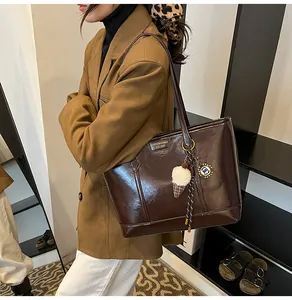 Détail du sac cabas brillant marron foncé avec logo en métal et pendentif peluche