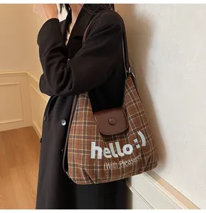 Detail of brown checkered tote bag with white hello text and leather magnetic flap closure