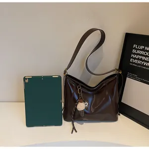 Detail of a large brown oil-wax leather tote bag with a plush ice cream charm for commute