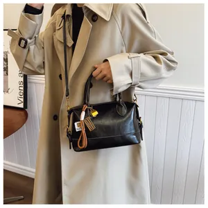 Detail of a black glossy Boston bag with gold hardware and tassel charm on a beige coat