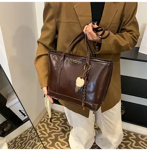 Détail d'un cabas en cuir brillant marron foncé avec plaque logo et charm en peluche