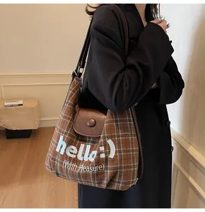 Brown plaid tote bag with leather flap and hello embroidery shown on model's shoulder