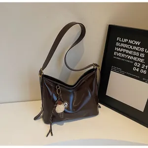 Detail of dark brown glossy leather hobo bag with adjustable strap and plush charm