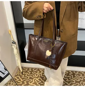 Détail du sac cabas marron foncé en cuir ciré avec logo doré et pendentif peluche