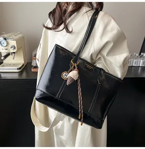 Détail du grand sac cabas noir brillant avec breloques porté par un mannequin
