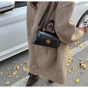 Detail of a vintage black leather crossbody bag with gold buckle on a brown coat