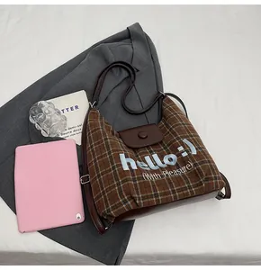 Detail of checkered tote bag featuring hello embroidery and brown leather trim accents