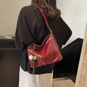 Elegant large burgundy leather tote bag with wide strap and pendant shown on model
