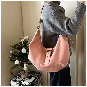 Pink suede crescent shoulder bag with metallic buckle strap shown on model's shoulder
