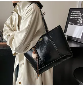 Détail d'un sac cabas en similicuir noir brillant avec pendentif et logo doré