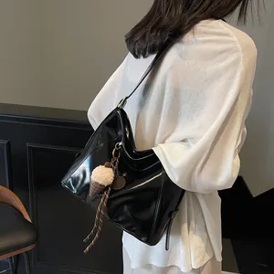 Glossy black crescent shoulder bag with pom-pom charm shown on a model for daily use