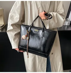 Détail d'un cabas en cuir verni noir avec logo doré et pendentif en peluche doux