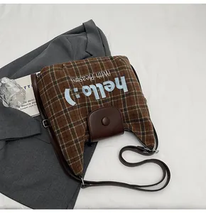 Detail of a brown plaid crossbody bag with blue embroidery and a vintage leather flap cover