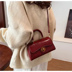 Detail of red patent leather handbag with gold metal twist lock and short handle