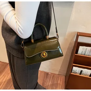 Dark green patent leather crossbody bag with gold lock shown on model indoors