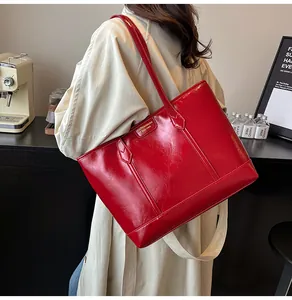 Détail du grand sac cabas en cuir verni rouge avec plaque dorée sur trench beige