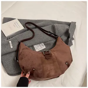 Detailed view of a brown crescent-shaped suede shoulder bag with a metal buckle decoration