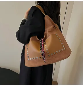 Close-up of brown suede bucket bag with hexagonal silver rivets and braided tassel