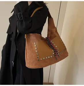 Macro detail of brown leather bucket bag with silver hexagonal rivets and woven rope charm