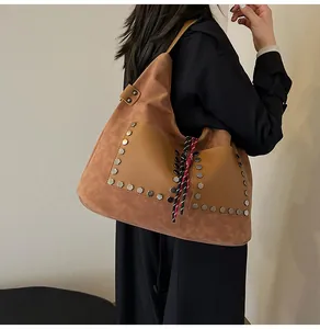 Close-up of brown suede hobo bag with silver hex rivets and braided tassel detail