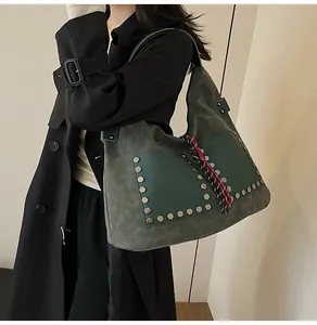 Detail of dark green suede hobo bag with silver hexagonal rivets and woven tassels