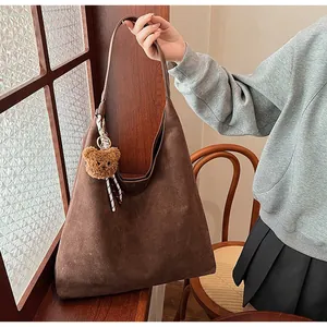 Detail of dark brown suede tote bag featuring a cute plush bear charm and wide strap