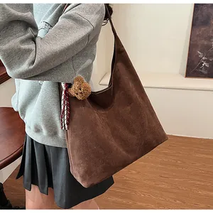 Detail of a large brown suede shoulder bag with a teddy bear charm and ribbon