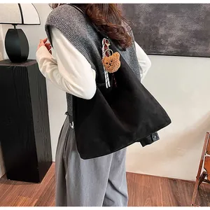 Detailed side view of black tote bag with plush bear charm and checkered scarf accent