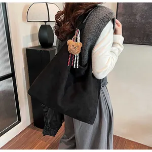Detail of large black suede tote bag with a cute brown plush bear charm accessory