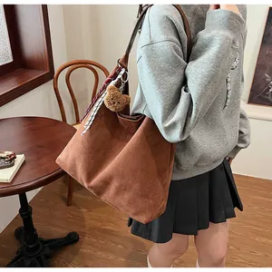 Close-up of a brown suede tote bag with a decorative silk scarf and cute bear pendant