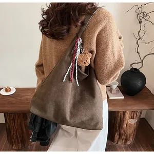Detail of brown suede tote bag featuring a striped ribbon and plush bear charm