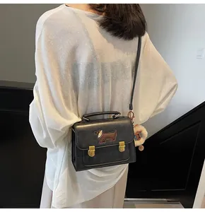 Detail of black square bag with brown dachshund embroidery and golden metal handle