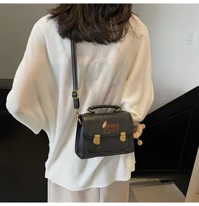 Detail of black PU leather handbag featuring a cute brown dachshund embroidery and metallic clasp